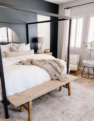 A dressed bed placed on a canopy bed frame in a styled room.png