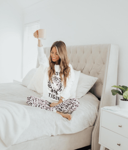 A woman sitting on a dressed Stearns and Foster mattress holding up a coffee cup.png