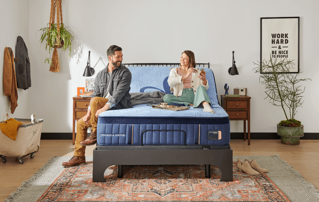 A couple sitting a lifted Lux Hybrid mattress set