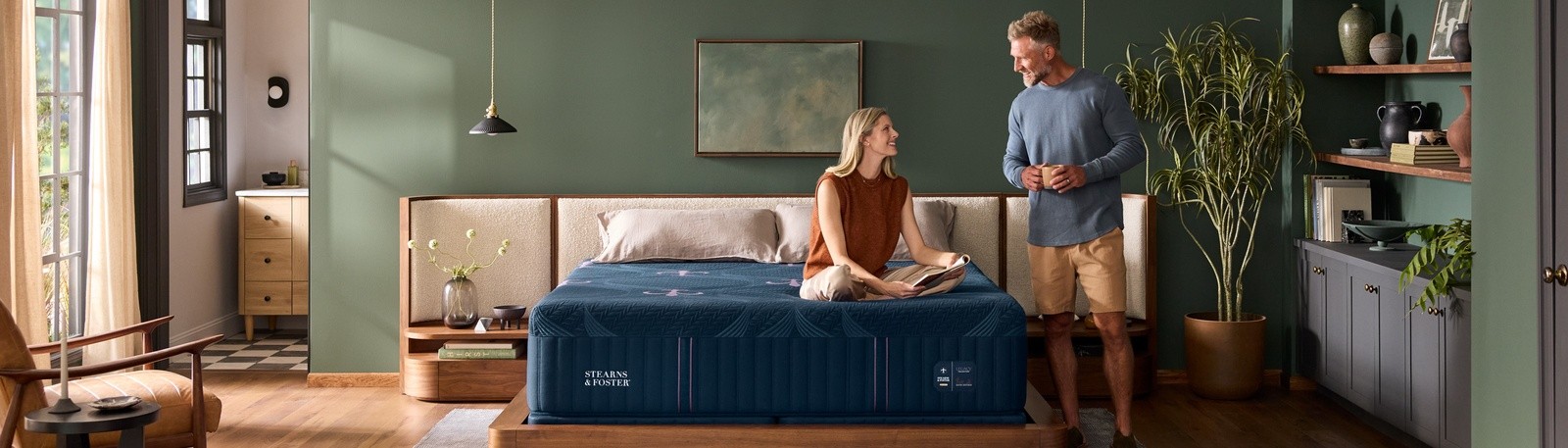 styled room with woman sitting on legacy mattress and man standing beside