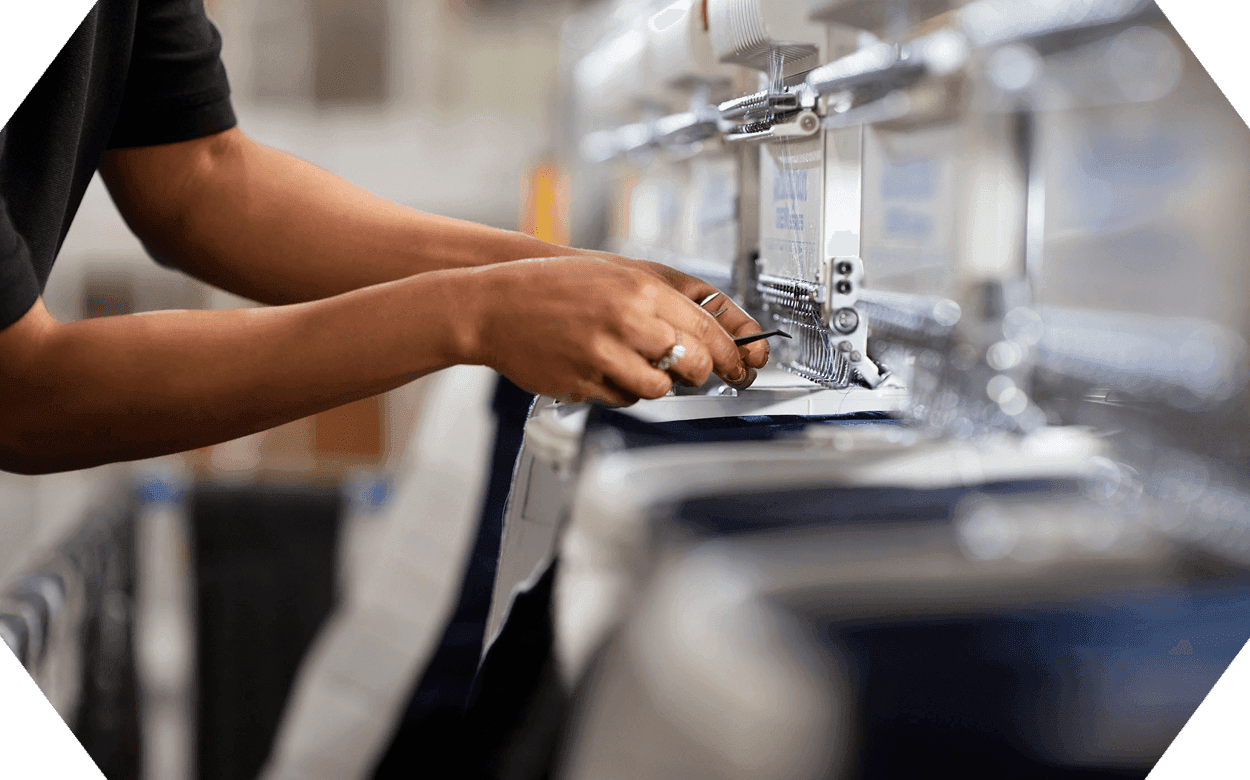 a hexogon shaped image displaying a plant worker sewing the boarder of a mattress together