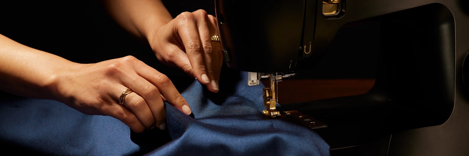 Hands feeding fabric under a sewing machine