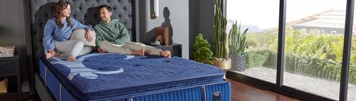 A man and a woman sitting on a Reserve mattress in a bedroom
