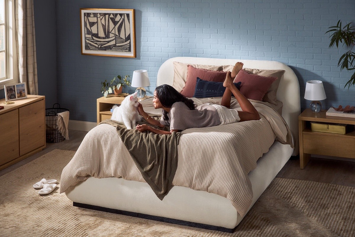 a dress bed with a woman laying on her stomach giving lovings to her white cat
